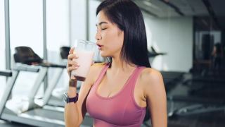 这位年轻美丽的亚洲女子在运动俱乐部的酒吧里喝奶昔。这位女士穿着运动胸罩，身材苗条。饮料是甜的，含有大量的蛋白质，对健康有好处。具有保健和美容理念的人。视频素材模板下载