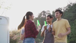 一群亚洲男女朋友在晚上一起参加户外聚会。朋友们带着幸福和微笑碰杯喝啤酒。旅行自然，露营用露营车。视频素材模板下载