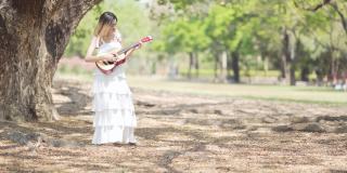 年轻迷人的女子在公园里弹吉他
