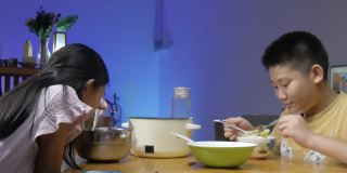 快乐的亚洲儿童享受晚餐涮涮锅或素喜烧在家里，led灯光背景。