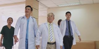 一组由医生、护士和助理组成的亚洲团队走过医院的走廊。有专业医疗经验的医生在室内行走，为拯救生命而工作。缓慢的运动。