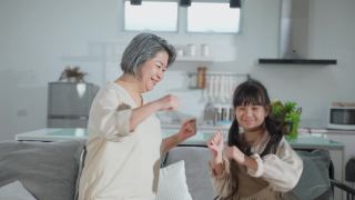 亚裔家庭小女孩和爷爷奶奶在客厅一起跳舞。孩子和老人带着笑脸运动，心情愉快。可爱的家庭和活动理念的快乐时刻视频素材模板下载