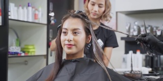年轻的亚洲美丽的女孩在沙龙改变发型和颜色。美发师在美容院给一位女士染发。女人笑着看着镜子。美发美容沙龙概念。