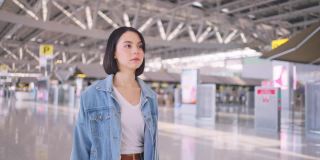 亚洲年轻迷人的女子乘客走在机场航站楼登机口与幸福和微笑的脸。那个女孩对乘飞机出国旅行感到兴奋。旅游业的概念。
