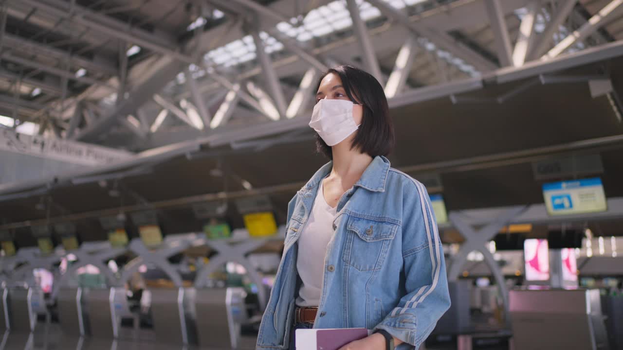 新冠肺炎疫情期间，佩戴口罩的女乘客在机场航站楼走向登机口，以防止感染新冠肺炎。飞机运输的新常态生活理念。