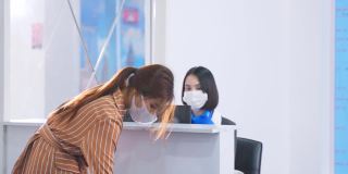 亚洲女性旅客将护照交给航空公司值机柜台的女工作人员，以便签发机票登机牌。女孩戴口罩预防冠状病毒大流行。新常态的生活方式