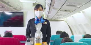 在飞行过程中，乘务人员在飞机上推服务车，为顾客提供服务。新常态下，空乘人员和所有乘客都要戴上口罩，以预防冠状病毒感染。