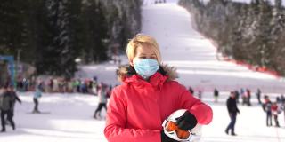 滑雪者戴着滑雪头盔和滑雪面罩，在斜坡上戴着外科口罩