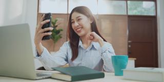 年轻美丽的亚洲女性与智能手机聊天使用笔记本电脑在家庭办公室工作