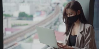 年轻美丽的亚洲女性戴着口罩使用笔记本电脑在家办公