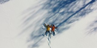 一对穿着彩色大衣的夫妇在厚厚的雪地上做蝴蝶的鸟瞰图
