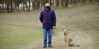 冬季，男性戴黑色防冠状病毒防护口罩，带着狗在森林附近的户外不动