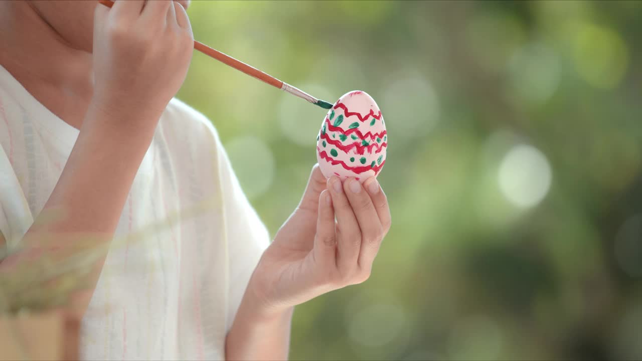 亚洲小女孩用画笔给复活节彩蛋上色。