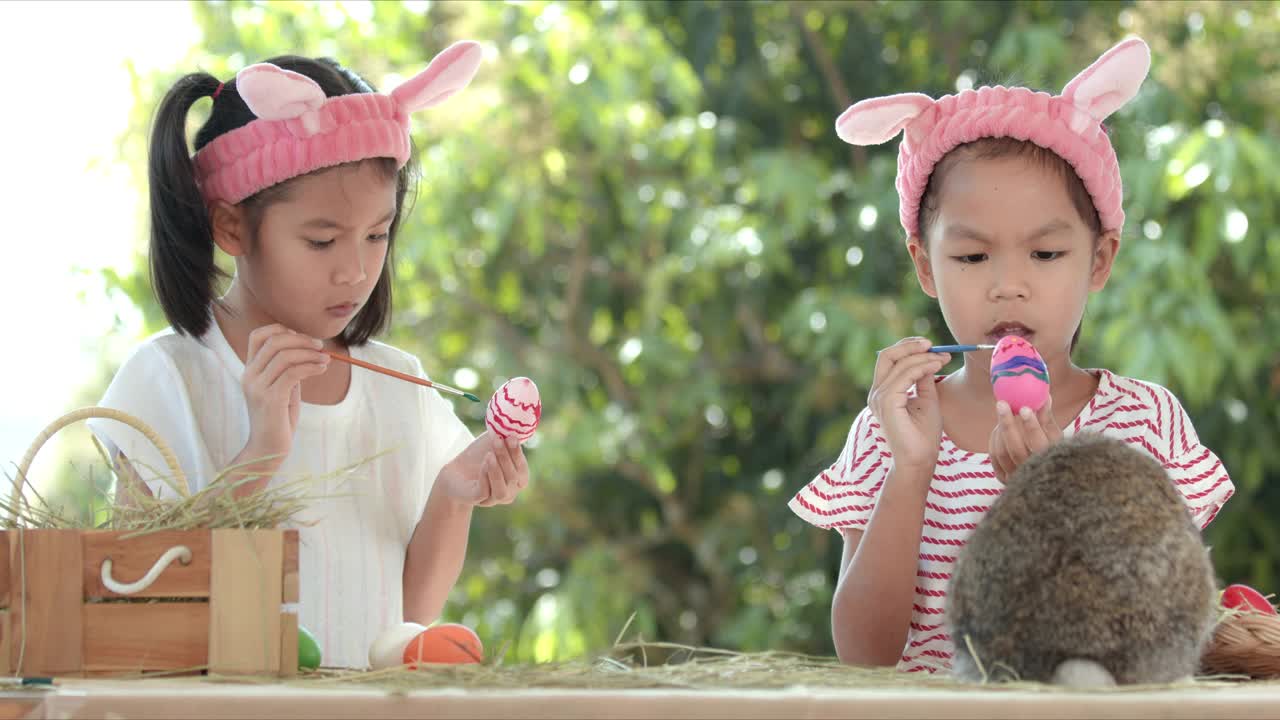 亚洲小女孩在桌子上的兔子旁边给复活节彩蛋上色。