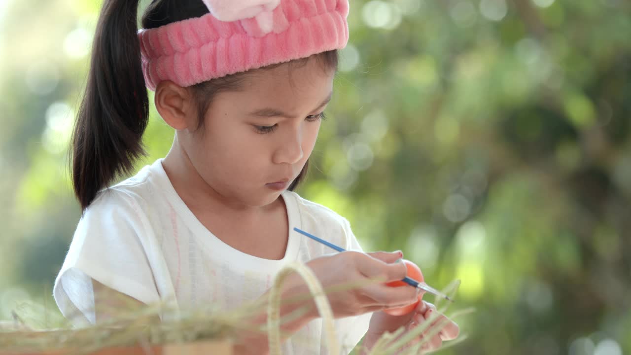 亚洲小女孩用画笔给复活节彩蛋上色。