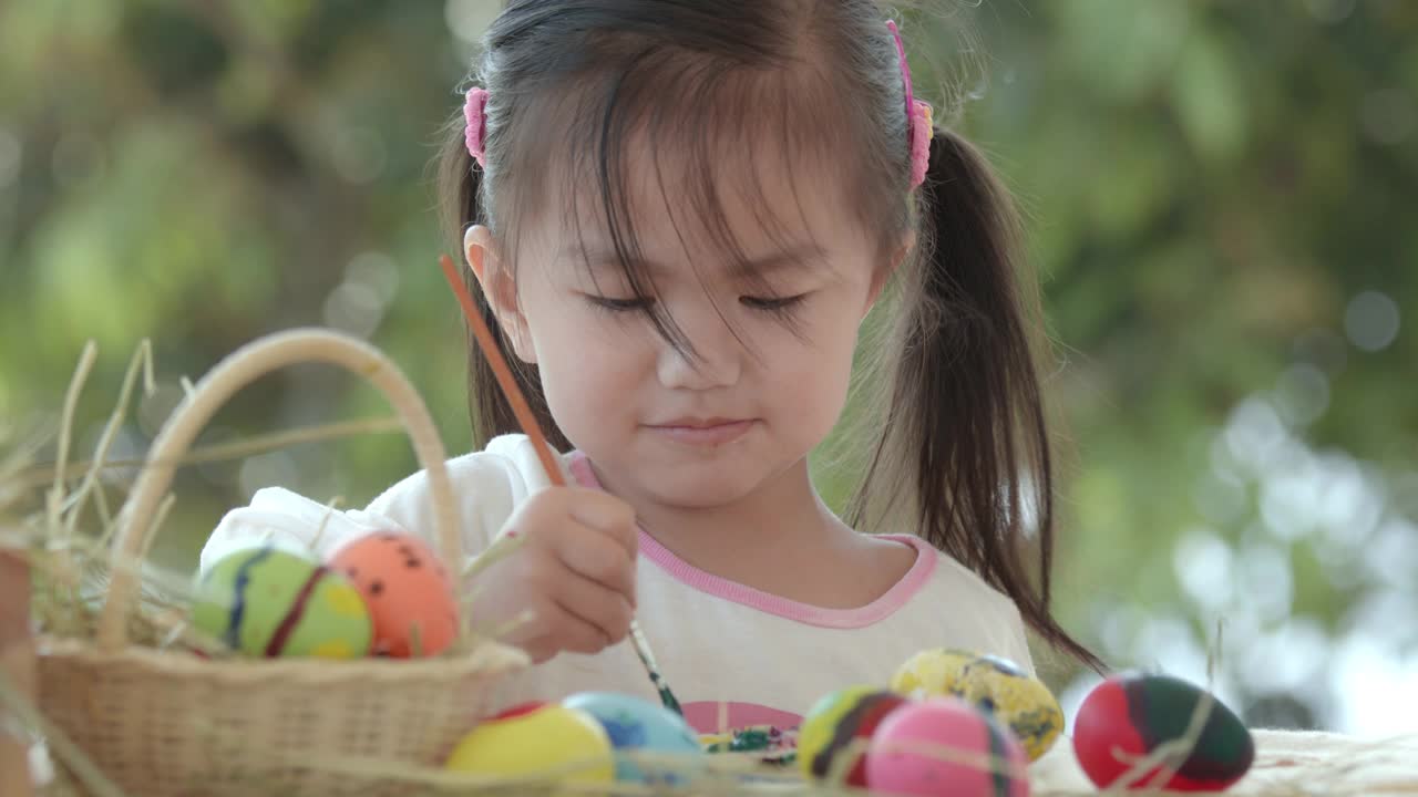 亚洲小女孩在书桌上用画笔和颜料给复活节彩蛋着色。