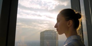透过摩天大楼的窗户看城市风景的女人——太阳光晕
