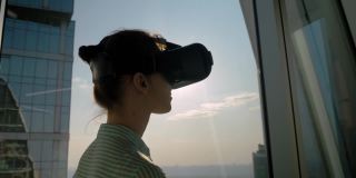 虚拟现实概念-年轻女子使用虚拟现实头盔对着摩天大楼的窗户