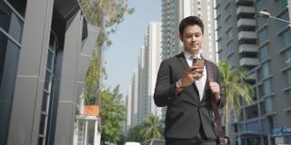 亚洲商人站在城市的街道上和他的同事在电话聊天，在你早上的通勤。