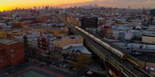 一列火车从车站出发，从布什威克俯瞰住宅区，俯瞰布鲁克林市中心和曼哈顿天际线的高空广角全景。无人机视频与向前摄像机运动。