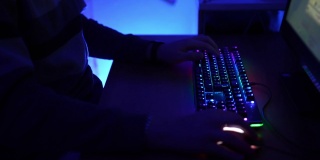 用蓝色霓虹灯照亮的暗室，懒人日夜玩在线游戏。特写的人的手指点击电脑键盘与光谱背光照明。视频网络空间和娱乐概念