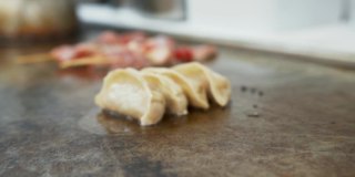 近距离观看饺子在餐厅厨房的热板上烹饪。在咝咝作响的铁板上煎炸的饺子和肉串