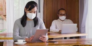 两个亚洲商务人士同事戴着防护口罩在家里办公，商业伙伴一起工作的新项目