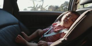可爱的亚洲蹒跚学步的小女孩坐在汽车座椅上，和家人一起旅行时睡觉。