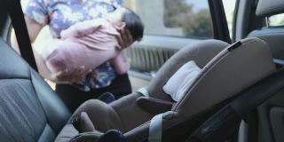 亚洲母亲抱着她的女儿，当她在车里睡觉，并把汽车安全带给她的女儿。可爱的亚洲蹒跚学步的女孩哭和困倦坐在汽车座位上。
