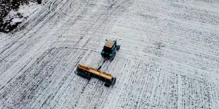 在冬季使用拖拉机在白雪皑皑的土地上用杀虫剂施肥的农机鸟瞰图