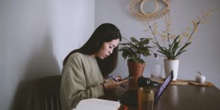 亚洲女性穿着休闲装在家加入桌面视频通话，在智能手机上做笔记，在家工作，远程工作的概念
