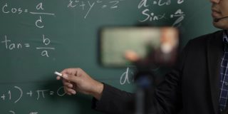 印度年轻教师男子戴着耳机通过智能手机进行在线视频会议直播。亚洲数学教师在线授课，供学生在线学习。