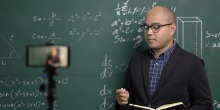 印度年轻教师男子通过智能手机进行在线视频会议直播。亚洲数学教师在线授课，供学生在线学习。