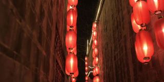 沿着右边的石墙向前走，穿过中国古庙的狭窄走廊。点燃了红灯笼，四处悬挂着照明灯。传统装饰，节日庆典