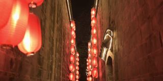 晚上在古庙狭窄走廊的石墙中间往前走。点燃了红灯笼，四处悬挂着照明灯。传统装饰，节日庆典