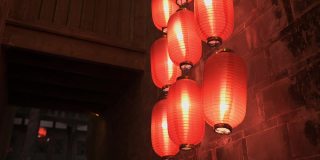 从下到上拍摄的中国寺庙的石墙和阳台在晚上。点燃的红灯笼悬挂在屋顶的柱子上，照亮灯光。传统装饰，东方节日庆典。