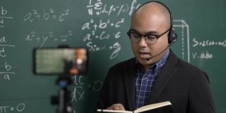 印度年轻教师男子戴着耳机通过智能手机进行在线视频会议直播。亚洲数学教师在线授课，供学生在线学习。