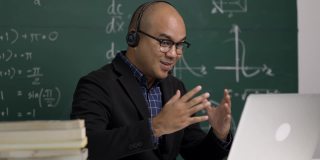 印度年轻教师男子戴着耳机坐着用笔记本电脑进行在线视频会议直播。亚洲数学教师在线授课，供学生在线学习。