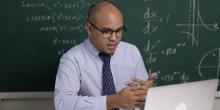 印度年轻教师男子坐着用笔记本电脑进行在线视频会议直播。亚洲数学教师在线授课，供学生在线学习。
