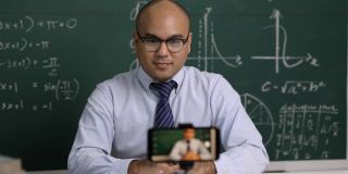 印度年轻教师男子坐着用智能手机进行在线视频会议直播。亚洲数学教师在线授课，供学生在线学习。
