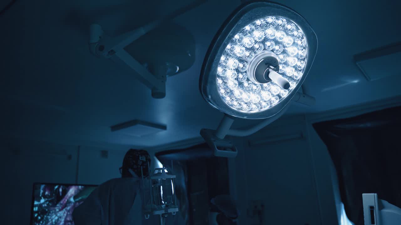 黑暗中的手术室。医用灯在手术室闪耀。医生在做手术时，要看屏幕。
