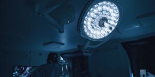 黑暗中的手术室。医用灯在手术室闪耀。医生在做手术时，要看屏幕。