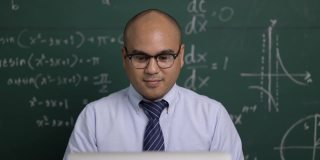 印度年轻教师男子坐着用笔记本电脑进行在线视频会议直播。亚洲数学教师在线授课，供学生在线学习。