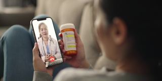 年轻的亚洲病人与她的医生在智能手机视频电话会议医疗应用远程医疗在线服务医院隔离社会距离在家概念。
