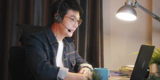 一名亚洲男子在家中使用笔记本电脑进行视频电话会议，工作到很晚