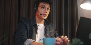 一名亚洲男子在家中使用笔记本电脑进行视频电话会议，工作到很晚