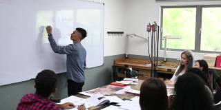 亚裔马来男讲师在教室里用白板给他的学生讲授珠宝设计课程