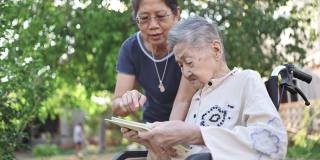 一位坐在轮椅上的残疾亚洲老人和她的年轻亚洲妇女在家里通过智能手机与家人进行视频聊天