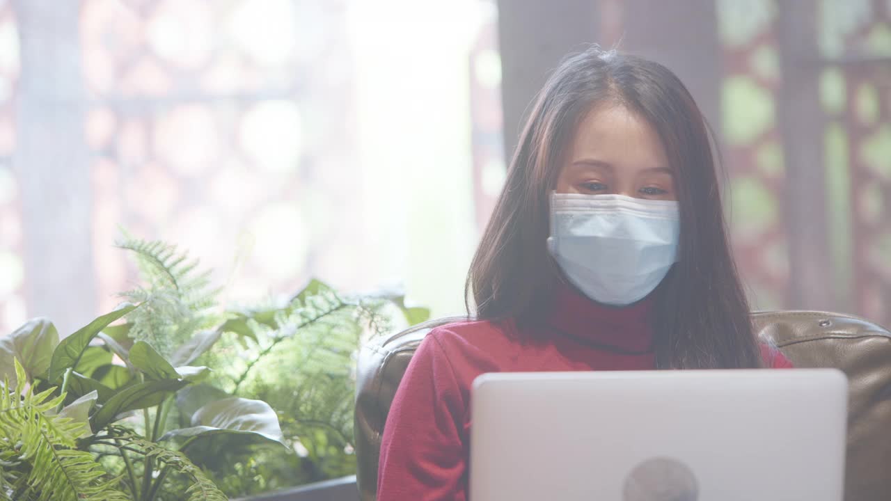 亚裔妇女穿着休闲服，戴着口罩以防感染冠状病毒。在网上搜索和申请工作。人们使用在线通讯，社交距离