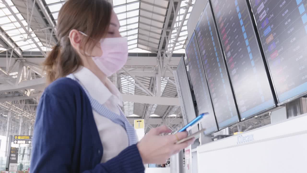 20-30岁的亚洲裔女性在新冠肺炎疫情下使用智能手机在机场旅行，新冠肺炎封锁和旅行重新开放后的新常态办公生活方式，